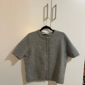 Grå kofta med korta ärmar - Säljer en mysig grå kofta med korta ärmar och silvriga knappar framtill. Perfekt för lager-på-lager under svalare dagar. Enkel och stilren design som passar till det mesta. Köpt på Zara förra året och älskar den den har bara blivit lite för liten!