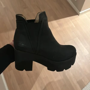 Svarta boots från Johnny Bulls med platå - Snygga svarta boots med hög platå och klack. Perfekta för att ge lite extra höjd och stil till din outfit. De har en enkel och stilren design som passar till många olika tillfällen.