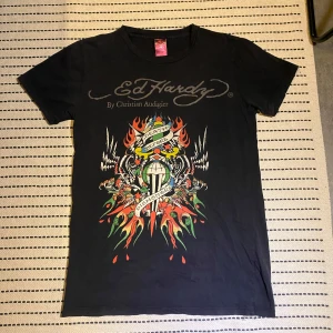 Svart t-shirt från Ed Hardy - Snygg svart t-shirt från Ed Hardy med färgglatt tryck och texten 'Death Before Dishonor'. Designad av Christian Audigier, perfekt för en cool och avslappnad stil. Kan skicka bild med plagget på. (Pris kan diskuteras)