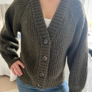 Olivgrön stickad kofta från Gina Tricot - Mysig olivgrön stickad kofta från Gina Tricot med stora knappar framtill. Perfekt för kyliga dagar med sin ribbade design och långa ärmar. En klassisk och bekväm tröja för alla tillfällen.