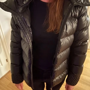 Svart pufferjacka från Colmar - Skitsnygg svart pufferjacka från Colmar med huva och dragkedja. Perfekt för kyliga dagar då den är jätte varm och skön! Jackan har en normal passform och är långärmad, vilket gör den idealisk för både höst och vinter. Knapot anvönd och i mycket fint skick!🥰