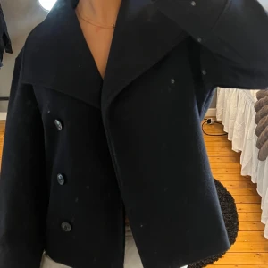 Marinblå kort kappa med knappar - Snygg marinblå kortkappa med stora knappar och bred krage. Perfekt för höst och vår. Jackan har en elegant och tidlös design som passar till många olika stilar.