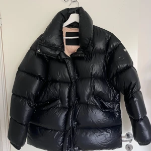 Svart pufferjacka från Peak Performance - Mycket bra skick förutom en lagad repa. Säljer pga kommer inte till användning.   Ganska stor i storleken, passar även en mindre L. Jackan har en glansig yta och är perfekt för kalla dagar. Den har en hög krage och stängs med dragkedja och knappar. 
