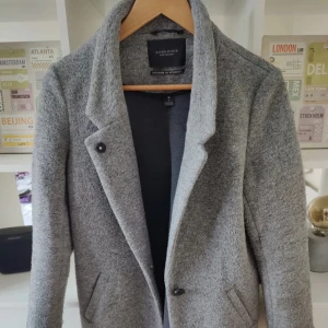 Grå kappa från Maison Scotch - Snygg grå kappa från Maison Scotch. Välanvänd men är fortfarande varm och skön. Har en lagkapp på insidan som inte syns när man har den på sig. Se bild. 