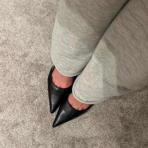 Svarta pumps med spetsig tå - Eleganta svarta pumps med spetsig tå och smal klack. Skorna har en justerbar rem med spänne för perfekt passform.