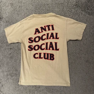 Beige t-shirt från Anti Social Social Club - Säljer en beige t-shirt från Anti Social Social Club med tryck i svart och rött på både fram- och baksidan. T-shirten har en klassisk passform och korta ärmar. Perfekt för en avslappnad stil., Size Xs, 199kr