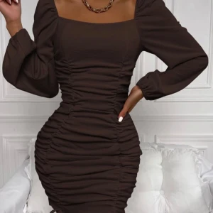 Brun klänning med rynkdetaljer - Elegant brun klänning med rynkdetaljer och långa ärmar. Den har en tight passform och en fyrkantig urringning som ger en stilren look.