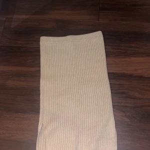 Beige ribbad kjol från NA-KD - Snygg beige ribbad kjol från NA-KD i storlek M. Kjolen har en stilren design med en liten slits på sidan. Tillverkad i ett mjukt, stretchigt och bekvämt material som passar bra till olika tillfällen.