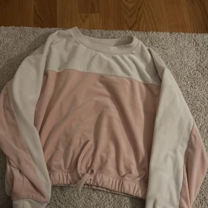 Rosa och vit tröja från Lindex - Säljer en söt rosa och vit tröja från Lindex i storlek 134/140. Tröjan har långa ärmar och en knytning i nederkanten för en justerbar passform. Perfekt för en avslappnad stil.