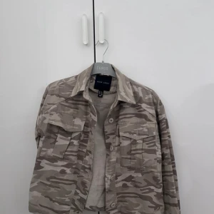 Beige camouflage overshirt från Eubus - Snygg beige overshirt i camouflage från Eubus. Perfekt för en avslappnad stil med knappar framtill och två bröstfickor. Passar bra till lager-på-lager och ger en cool look.