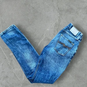 Blåa nudie jeansbyxor - Snygga blå jeansbyxor av nudie. De har en normal passform och är perfekta för en avslappnad stil. Byxorna har en dragkedja och knapp framtill.