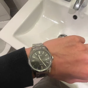  klocka  - Snygg och stilren klocka  med silverfärgad länk och svart urtavla. Klockan har datumvisning och klassisk design som passar perfekt för alla tillfällen.