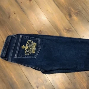 Mörkblå jeans med guld krona - Snygga mörkblå jeans med en guldfärgad krona på bakfickan. Dom är i storlek s/m och är lågmidjade och raka/ lite bootcut. Pris kan diskuteras