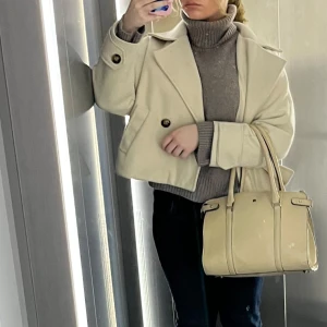 Beige kappa från Missäy - Snygg beige kappa från Missäy med stora knappar framtill. Den har en klassisk krage och två fickor. Perfekt för kyligare dagar.