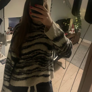 Zebramönstrad stickad tröja - Säljer en mysig zebramönstrad stickad tröja i svart och beige. Tröjan har en hög krage och långa ärmar, perfekt för kyliga dagar. Den har en loose passform som ger en avslappnad look. Den är aldrig använd utan bara testad. Pris går att diskutera, kontakta gärna vid frågor eller annat😊💗