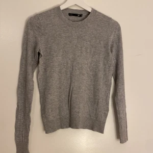 Grå stickad tröja från H&M - Säljer en stilren grå stickad tröja. Perfekt för kyligare dagar med sin mjuka och bekväma passform. Tröjan har långa ärmar och rund halsringning.
