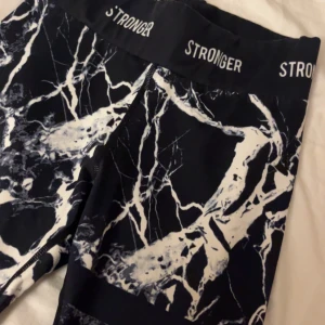 Svarta leggings med marmorprint från Stronger🖤🤍 - Snygga svarta leggings med ett unikt marmorprint i vitt från Stronger. Perfekta för träning eller en avslappnad dag. De har en elastisk midja med logotypen 'STRONGER' runtom. Använd fåtal gånger! Nypris:799❤️❤️