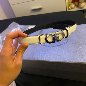 Vit skinnbälte med silverdetaljer - Snyggt vitt skinnbälte med en elegant silverfärgad spänne från Ferragamo. Perfekt för att ge en stilren touch till din outfit. Passar bra till både jeans och klänning.