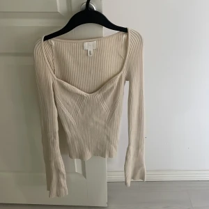 Beige ribbad topp från H&M - Säljer en stilren beige ribbad topp från H&M med långärmad design och v-ringad hals. Perfekt för en chic och bekväm look. Passar utmärkt till både jeans och kjol.