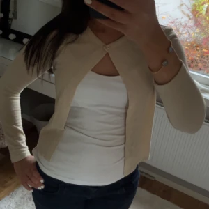 Beige kofta med knappdetalj - Säljer en stilren beige kofta med en enkel knapp framtill. Andvänt några få gånger och den kommer inte riktigt till användning längre💕