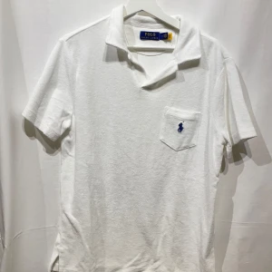 Vit kortärmad pikétröja från Ralph Lauren - Snygg vit pikétröja från Ralph Lauren med klassisk krage och korta ärmar. Tröjan har en bröstficka med det ikoniska blå broderade logotypen. Perfekt för en stilren och avslappnad look. Piken är knappt använd och Materielet är frotté, modellen är 180cm