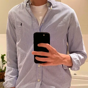 Randig skjorta från Ralph Lauren - Snygg randig skjorta från Ralph Lauren i blått och vitt. Skjortan har en klassisk krage och knappar framtill. Den är långärmad och har en broderad logotyp på bröstet. Perfekt för en stilren look.