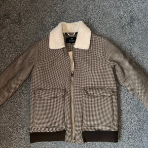 Rutig jacka med teddyfoder från Matinique - Säljer en snygg rutig jacka från Matinique i herrstorlek Large. Jackan har ett mjukt teddyfoder och en krage i samma material. Den är utrustad med dragkedja och har praktiska fickor framtill. Perfekt för kyligare dagar! 