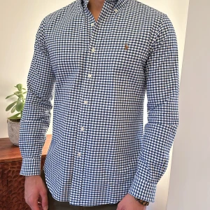 Rutig skjorta från Ralph Lauren - Snygg rutig skjorta från Ralph Lauren i blått och vitt. Skjortan har långa ärmar och knappar framtill. Perfekt för en stilren look.  Tvättat och pressad på kemtvätt inför försäljning 100% bomull Felfritt skick  Storlek S, dock stor i storleken och närmare medium Väger 77-78kg och är 179cm lång 