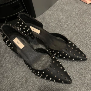 Nelly  - Snygga svarta pumps från Nelly med spetsig tå och coola nitar över hela skon. Perfekta för att ge en edgy touch till din outfit. Använda 1 gång så i princip nya! 