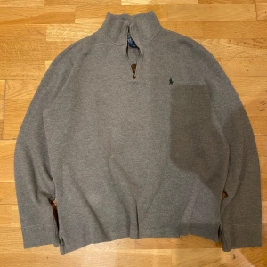 Grå tröja med dragkedja från Polo Ralph Lauren - Säljer en stilren grå tröja från Polo Ralph Lauren med halv dragkedja och broderad logga på bröstet. Perfekt för en avslappnad och snygg look.