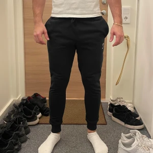 Svarta mjukisbyxor från Gymshark - Säljer ett par svarta mjukisbyxor från Gymshark. Byxorna har en tight passform med snörning i midjan och en diskret logga på benet. Perfekta för träning eller en avslappnad dag hemma.