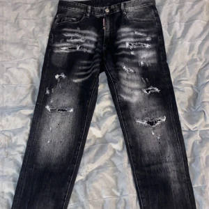 Svarta jeans från Dsquared2 - Snygga svarta jeans från Dsquared2 med slitna detaljer och en cool, tvättad look. De har en klassisk femficksdesign och knappgylf. Perfekta för en trendig och avslappnad stil.
