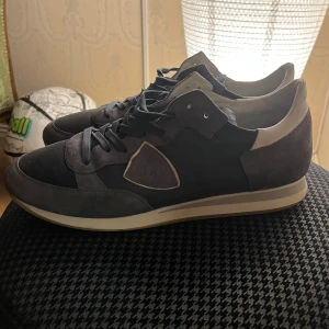 Grå sneakers från Philippe Model - Snygga grå sneakers från Philippe Model med en stilren design. Skorna har snörning och en bekväm sula i gummi. Perfekta för en avslappnad stil.