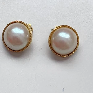 Guldörhängen med pärlor - Eleganta guldörhängen med stora vita pärlor. De har en klassisk design med clip-on fäste, vilket gör dem enkla att bära utan hål i öronen. Perfekta för att ge en sofistikerad touch till din stil. Okänd metall 