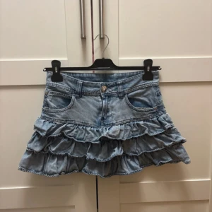 Blå jeanskjol med volanger - Snygg blå jeanskjol med flera lager volanger. Kjolen har är i barnstorleken 164 men skulle säga att den passar xxs/xs ungefär☺️ Den har tyvärr ett litet hål som man kan se på bild 3 men det går nog att sy ihop så att de knappt syns!!