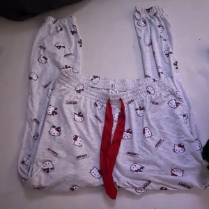  Hello Kitty pyjamasbyxor - Mysiga gråa pyjamasbyxor med Hello Kitty-motiv och röd snörning i midjan. Perfekta för en avslappnad hemmakväll. Använt en gång.