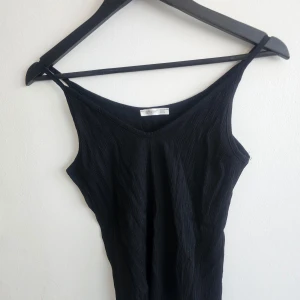 Svart ribbad linne från Amber - Snygg svart ribbad linne från Amber med smala axelband och v-ringning. Perfekt för en stilren look. Linnet har en enkel och elegant design som passar till många tillfällen.