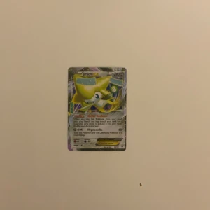 Jirachi EX Pokémonkort - Säljer ett Jirachi EX Pokémonkort med holografisk design. Kortet har en färgglad och glittrande yta med Jirachi i fokus. Perfekt för samlare eller Pokémon-entusiaster som vill utöka sin kortsamling.