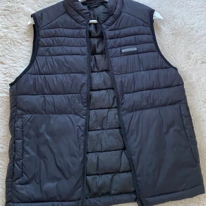 Svart dunväst med dragkedja - Snygg svart dunväst med dragkedja framtill. Perfekt för kyligare dagar. 