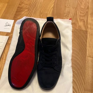 Mörkblåa skor från Christian Louboutin - Snygga mörkblåa sneakers från Christian Louboutin med den ikoniska röda sulan. Skorna har snörning och är tillverkade i mocka, vilket ger en lyxig känsla. Perfekta för att ge din outfit en exklusiv touch.