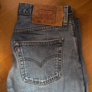 Levi's 501 Jeans - Klassiska Levi's 501 jeans i en snygg blå tvätt. Dessa jeans har en rak passform och är tillverkade i slitstarkt denim. Perfekta för en avslappnad stil med den ikoniska Levi's-lappen på baksidan. Mått finns att skicka :)