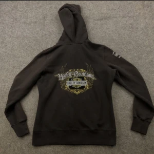 Unik hoodie från Harley-Davidson - Snygg mörkbrun hoodie med stort Harley-Davidson-tryck på ryggen & ena ärmen 💓. Detaljerna i trycket ger en cool och unik look! Lite y2k , 2000-tals. Knappt använd så bra skick 🙏🏼