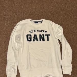 Vit sweatshirt från GANT - Säljer en stilren vit sweatshirt från GANT med texten 'New Haven' tryckt på bröstet. Tröjan har långa ärmar och en klassisk rund halsringning. Perfekt för en avslappnad look.
