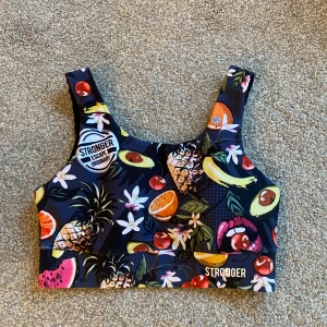 Färgglad sporttopp från Stronger - Säljer en färgglad sporttopp från Stronger med fruktmönster. Toppen har breda axelband och en elastisk kant nedtill för extra stöd. Perfekt för träning och ger en glad touch till din outfit. 