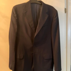 Svart kavaj från Massimo Dutti - Elegant svart kavaj från Massimo Dutti med klassisk design. Kavajen har två knappar framtill och är perfekt för en stilren look. Passar utmärkt till både formella och semi-formella tillfällen.