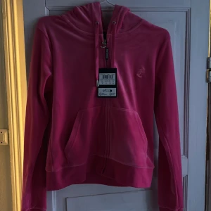 Rosa hoodie från Juicy Couture - Säljer en snygg rosa hoodie från Juicy Couture i modellen Robertson. Den har en dragkedja framtill och en justerbar huva med snören. Aldrig använd, prislapp kvar