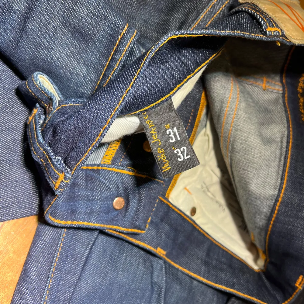 Säljer ett par mörkblå jeans från Nudie Jeans med klassisk femficksdesign och orange sömmar. Perfekta för en stilren look. Model: grim tim, storlek 31/32, finns små fläckar som ej syns på en distans. Farkut & Housut.