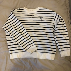 Randig tröja från Bisous - Säljer en vit och svart randig tröja från Bisous med ett litet tryck av en rosett och texten 'Bisous 1921' på bröstet. Tröjan har långa ärmar och en rund halsringning. Perfekt för en avslappnad stil.