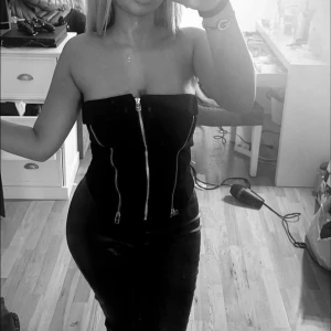 Svart axelbandslös topp med dragkedja - Trendig svart axelbandslös topp med dragkedja framtill. Perfekt för en kväll, toppen har en tight passform som framhäver formerna. Passar xs och S stressigt material.