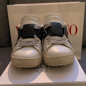 Valentino open  - Snygga Valentino sneakers i vitt med en bred svart rem över snörningen. Skorna har en klassisk design med rund tå och platt sula. Perfekta för en stilren look. Dessutom får men med box,påse till skorna och snören
